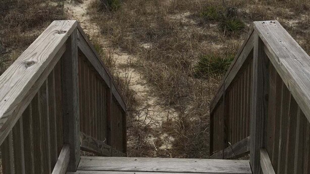Una pasarela de madera que conduce a una playa bajo un cielo nublado.