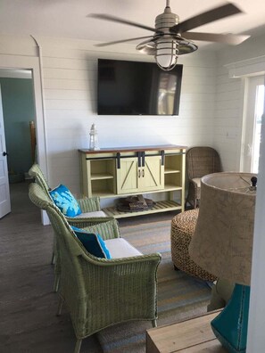 A room with wicker furniture, a ceiling fan, a television, and a lamp.
