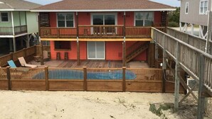 Una casa de dos pisos con un balcón, una terraza de madera y una piscina.
