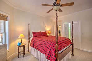 Una cama con dosel con un edredón a cuadros rojo y negro, una mesita de noche de madera con una lámpara y un ventilador de techo.