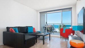 A modern living room with a black sofa, a red chair, and a large window offering a view of the sea. - A modern, Coastal Unit in Shoal Bay! (Shoal Bay)