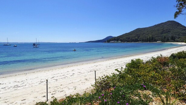A beach with clear blue water, boats, and a mountain in the background. - A modern, Coastal Unit in Shoal Bay! (Shoal Bay)