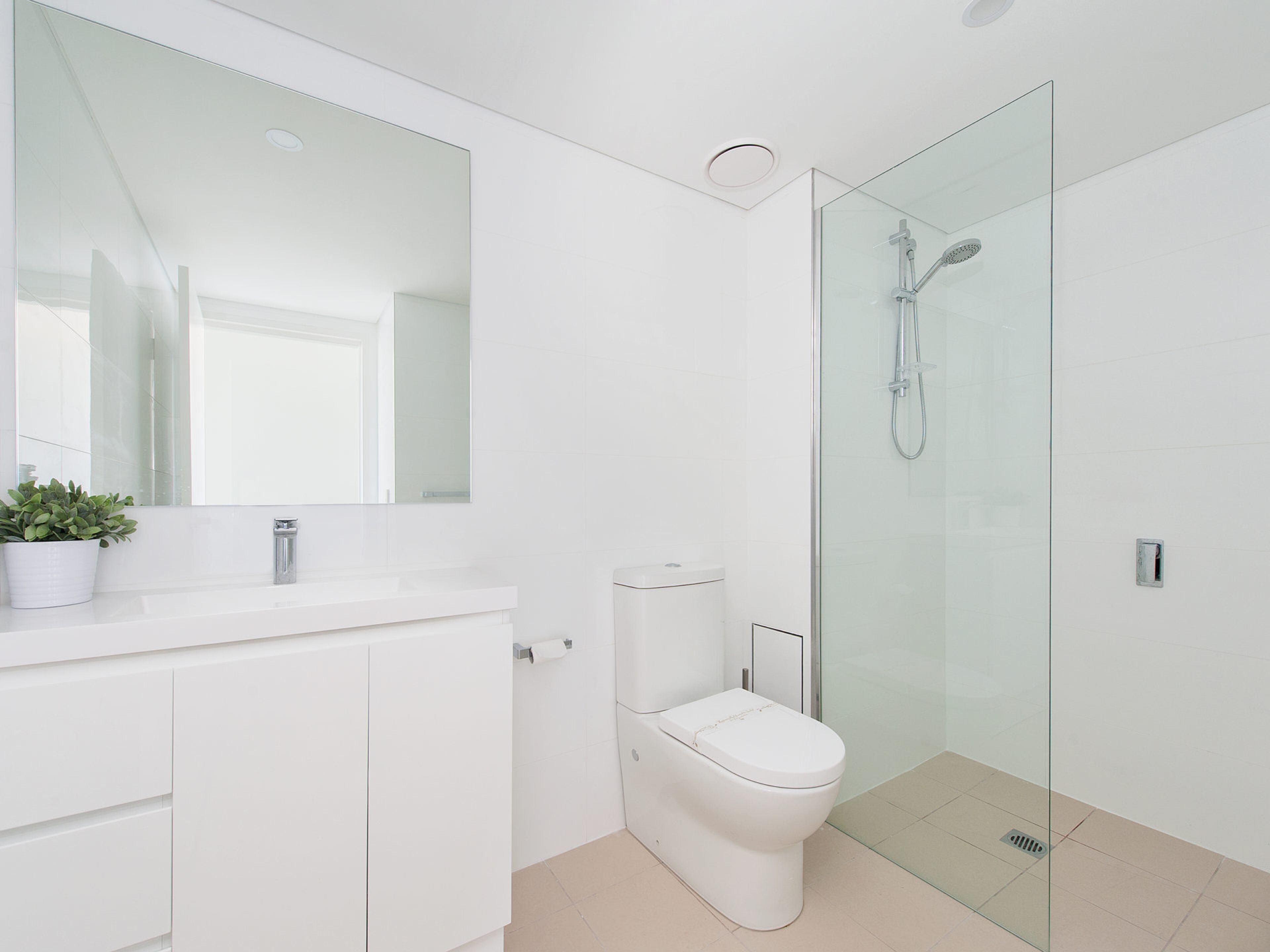 A modern bathroom with a glass shower enclosure, a toilet, and a white sink with a mirror above.