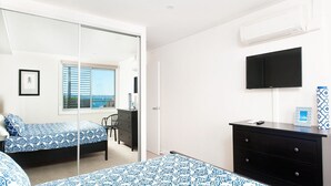 A bedroom with two beds, a desk, a chair, a TV, and an air conditioning unit. - A modern, Coastal Unit in Shoal Bay! (Shoal Bay)