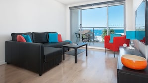 Un soggiorno moderno con un divano nero, un tavolino e una poltrona rossa. Un'ampia finestra offre vista sul mare.