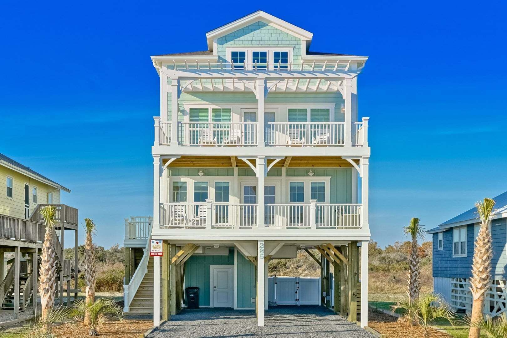 A multi-story beachfront house with balconies, a covered entryway, and a garage.