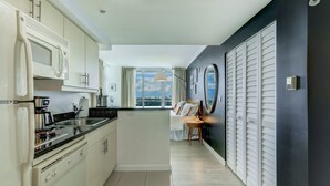 A modern kitchen with a stove and sink, a dining area with a table and chairs, and a bedroom with a bed and a view of the city. - Corner Deluxe Studio w/ City View Free Park & Pool (Miami)