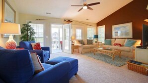 A living room with a blue sofa, a beige sofa, a coffee table, a ceiling fan, and a television. - Charming oceanfront retreat, Sea Shanty / 153 Marlin, with 3 beds in Holden Beach. (Holden Beach)