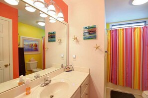 A bathroom with a white sink, a mirror, and a colorful striped shower curtain. - Charming oceanfront retreat, Sea Shanty / 153 Marlin, with 3 beds in Holden Beach. (Holden Beach)