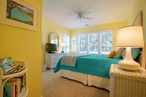 A bedroom with a bed, a television, a lamp, a wicker chair, and a bookshelf. - Charming oceanfront retreat, Sea Shanty / 153 Marlin, with 3 beds in Holden Beach. (Holden Beach)