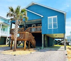A two-story house with a wooden deck and a palm tree.