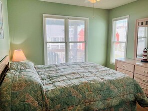 A bedroom with a bed, dresser, lamp, and large windows.