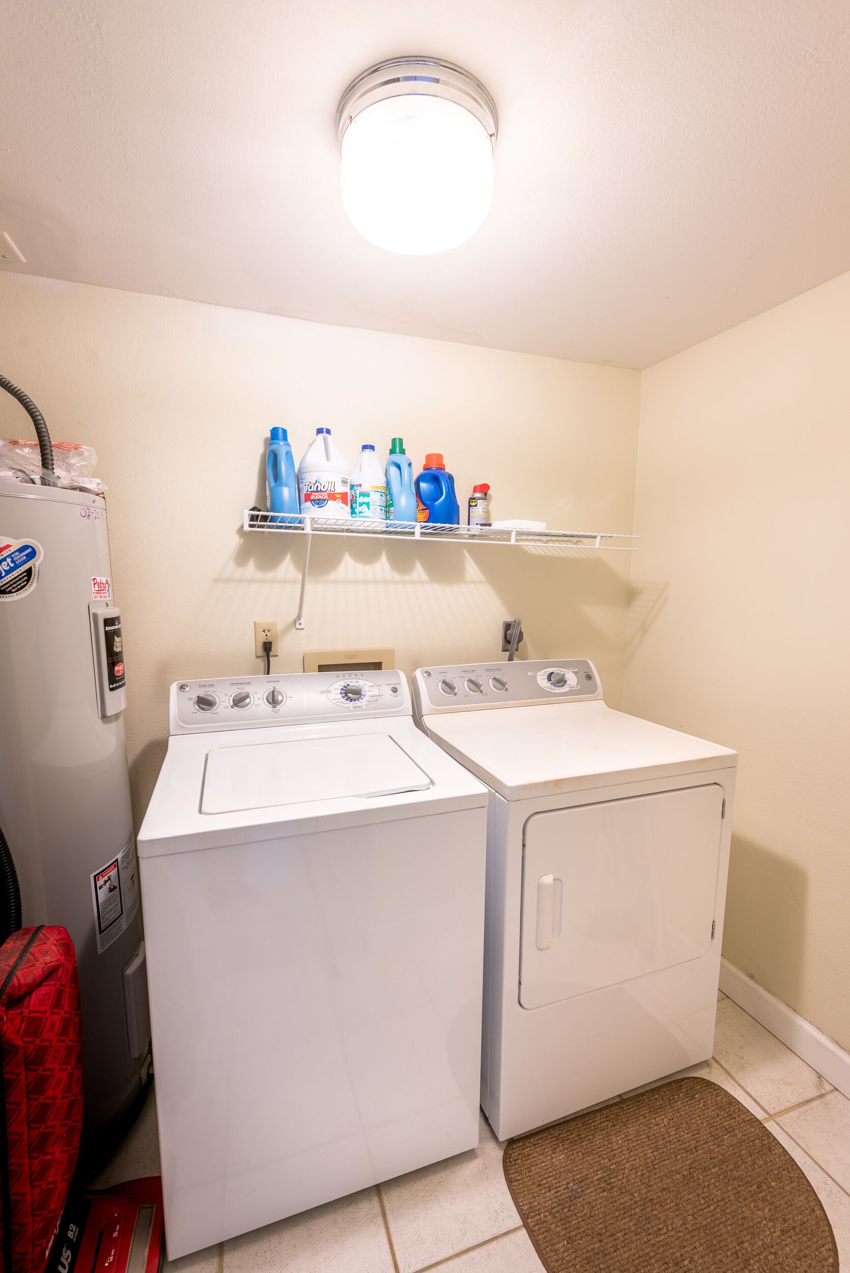 Une buanderie équipée de deux machines à laver et deux sèche-linge à chargement frontal, d’une étagère où sont rangées les bouteilles de lessive et d’un panier à linge rouge.