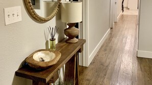 A hallway with a wooden console table, a mirror, a lamp, and a door leading to a kitchen area.