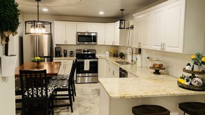 A modern kitchen with white cabinets, stainless steel appliances, a granite countertop, and a dining area with a patterned tablecloth.