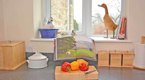 A kitchen counter with a book, a cutting board with peppers, a white ceramic pot, and wooden storage boxes.