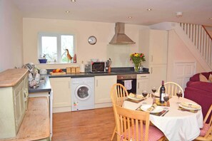 A compact kitchen with a washing machine, a dining table set for two, and a dining area with a red sofa.