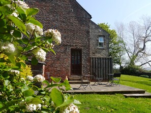 A rustic stone building with a wooden door, a small window, and a patio with outdoor furniture.