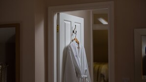 Une robe blanche est suspendue à une porte dans une pièce qui contient un miroir et un interrupteur sur le mur.
