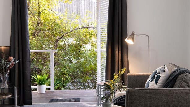 Un salon moderne avec un canapé, une lampe sur pied, une table basse et une vue sur la verdure à l’extérieur.