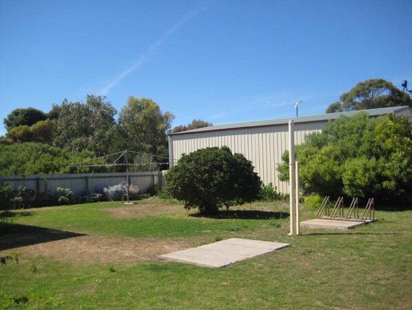 A fenced backyard with a grassy area, a concrete slab, and a tall building in the background.