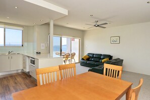 A modern kitchen with a dining area, a sofa, and a ceiling fan.