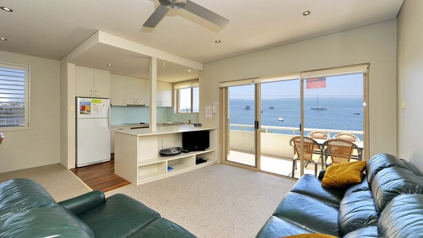 A modern living room with a sofa, a television, and a balcony with a view of the sea. - Del Rae, Unit 12/25 Shoal Bay Road - North-facing apartment overlooking the Bay (Shoal Bay)