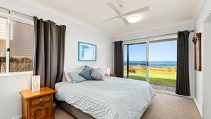 Enjoy ocean views from the large window in this serene bedroom, featuring a comfortable bed, a nightstand, and a ceiling fan.
