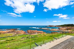 A coastal landscape with rocky terrain, grassy areas, and a clear blue sky.