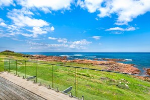 A coastal landscape with a clear sky, rocky shoreline, and a grassy area with a wooden deck. - Birubi Beach getaway at Anna Bay (Anna Bay)
