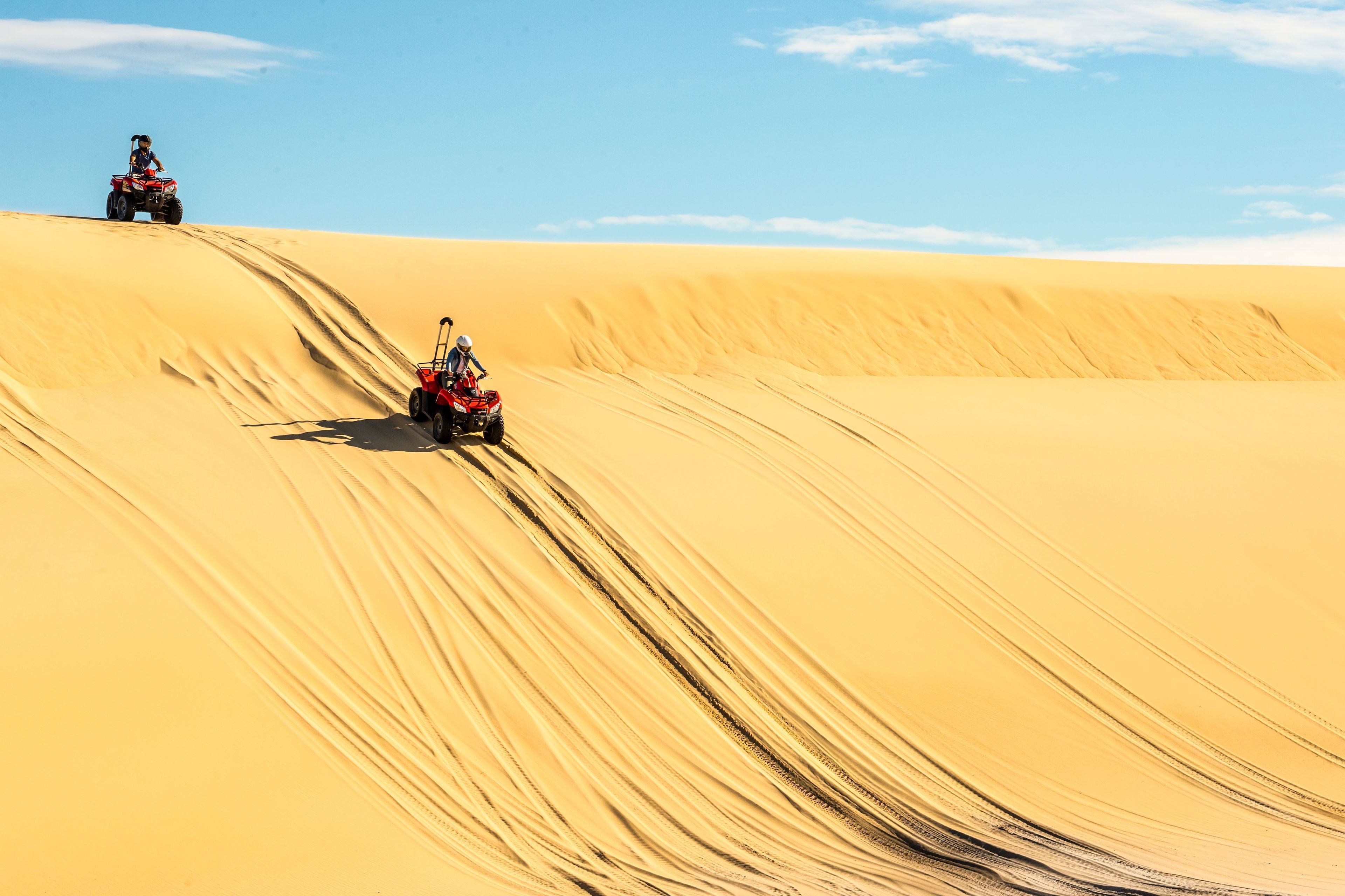 Wüstenlandschaft mit Sanddünen und einem roten Quad, das in Bewegung ist.