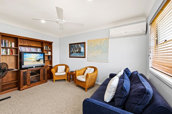 A living room with a television, bookshelves, two wicker chairs, a blue sofa, and a ceiling fan.