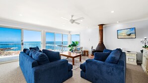 Uma sala de estar com uma vasta vista para o oceano, um ventilador de teto e uma lareira.