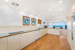 A modern kitchen with white cabinetry, a wooden countertop, and a view of the sea through large windows. - Birubi Beach getaway at Anna Bay (Anna Bay)