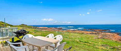 A deck with a table and chairs overlooking a rocky coastline and ocean.
