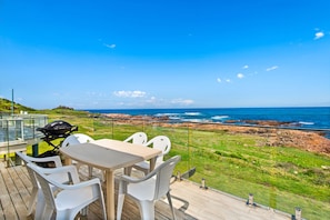 Een terras met tafel en stoelen met uitzicht op een rotsachtige kustlijn en de oceaan.