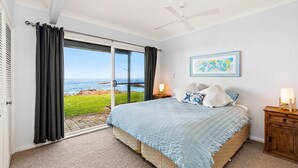 Quarto com uma cama grande, vista para o oceano, ventoinha no teto e quadro na parede.