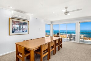 Een eetruimte met een houten tafel en stoelen, een plafondventilator en een groot raam met uitzicht op de oceaan.