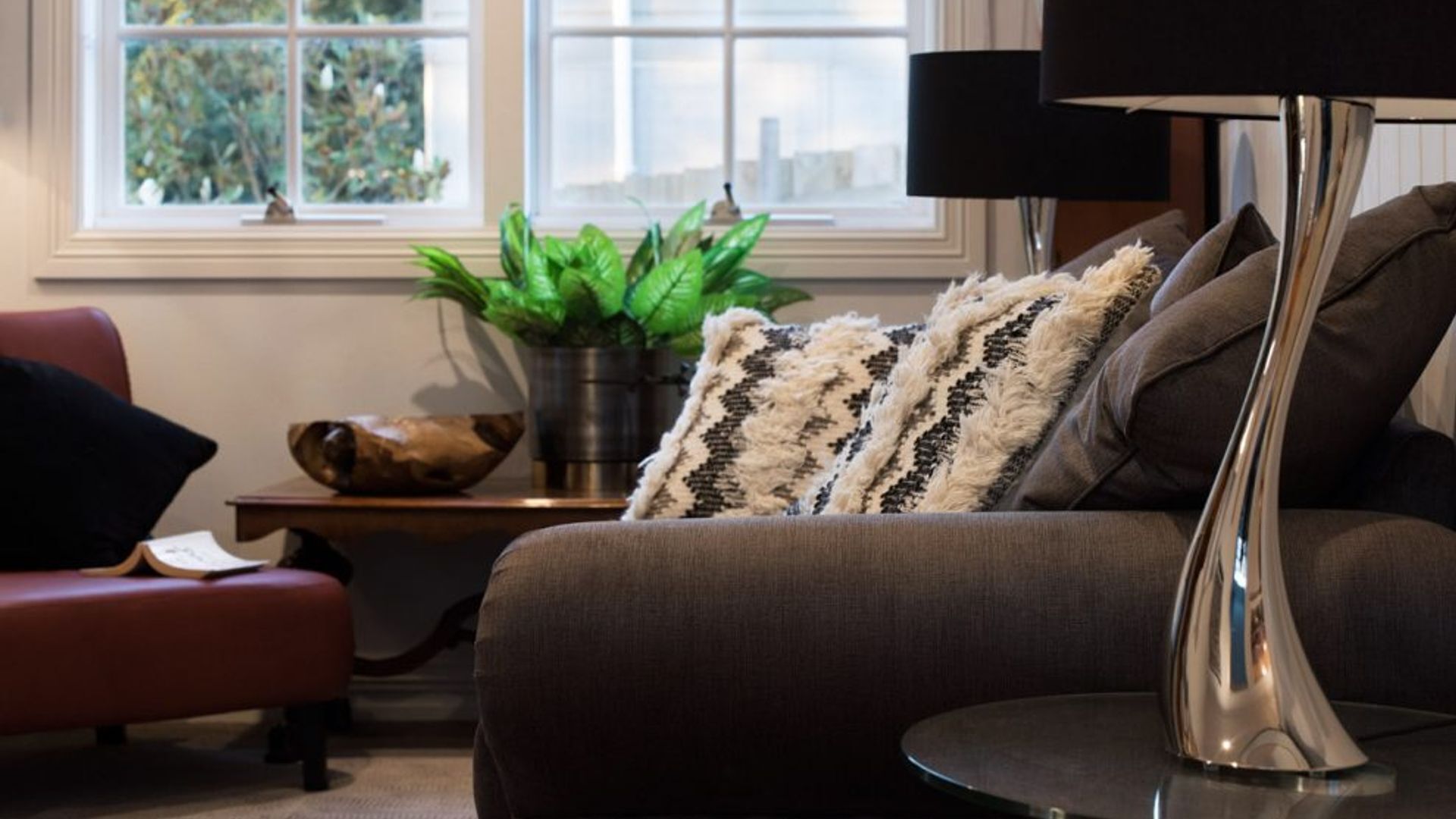 A modern living room with a sofa, a side table, a lamp, and a window with a view of trees.