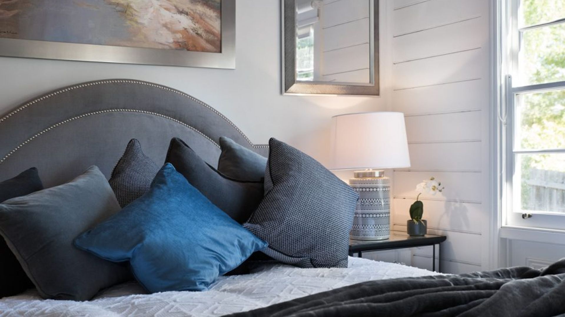 Ein Schlafzimmer mit Bett, Kissen, einer Nachttischlampe und einem Fenster.