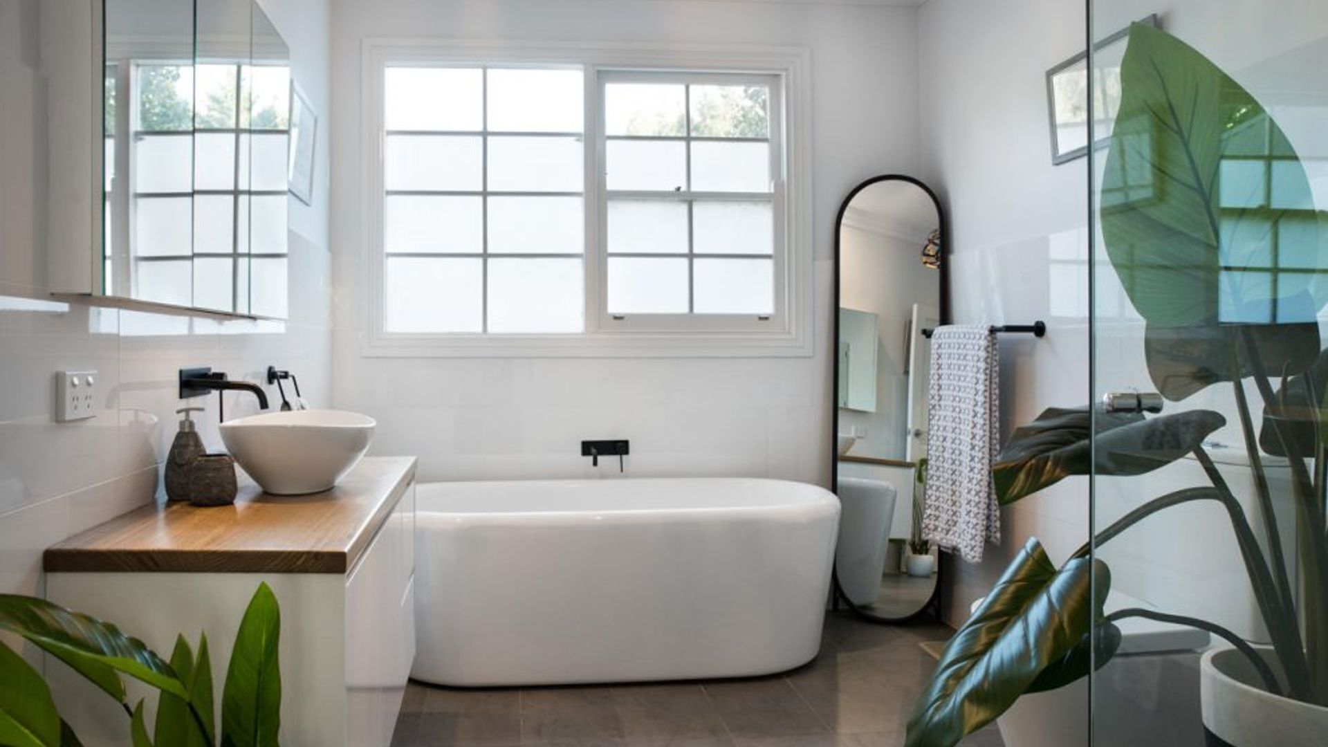 Ein modernes Badezimmer mit freistehender Badewanne, einem großen Fenster und einem Spiegel.