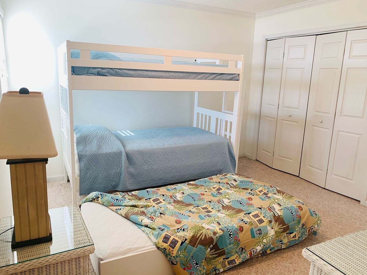 A bunk bed with a blue mattress, a patterned pillow, a lamp, and a wicker table.