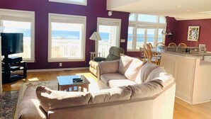 Een woonkamer met een bank, een televisie en een eethoek met stoelen en een tafel.