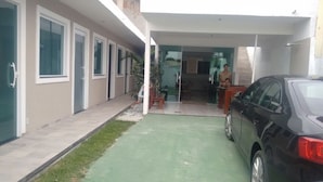 Un edificio moderno con un acceso cubierto, un coche estacionado afuera y un pequeño espacio exterior con mesas.