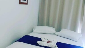 Una cama bien hecha con ropa de cama blanca y azul, una toalla doblada y un cuadro en la pared.