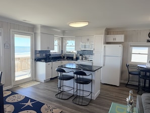 A kitchen with a central island, bar stools, a refrigerator, and a view of the beach. - Experience beachfront bliss at Sea It All in Holden Beach, NC, perfect for 6 guests. (Holden Beach)