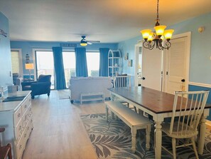 Une pièce comprenant une table à manger, des chaises, un canapé, un ventilateur de plafond et une vue sur la plage.
