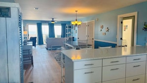 A kitchen with a central island, a dining area with a table and chairs, and a living room with a sofa and a coffee table. - Enjoy oceanfront bliss at When Pigs Fly, a spacious 4BR gem in Holden Beach, NC. (Holden Beach)