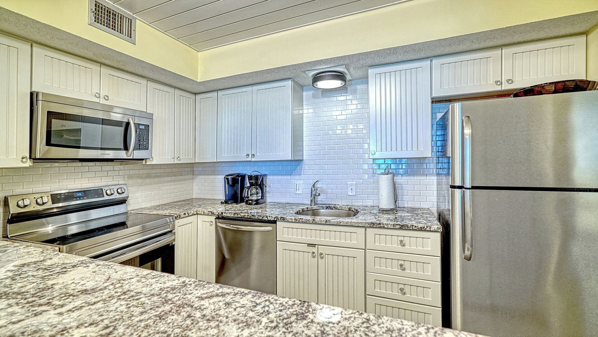 A kitchen with white cabinetry, a stainless steel refrigerator, a microwave, an oven, a coffee maker, and a sink.