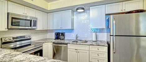 A kitchen with white cabinetry, a stainless steel refrigerator, a microwave, an oven, a coffee maker, and a sink.